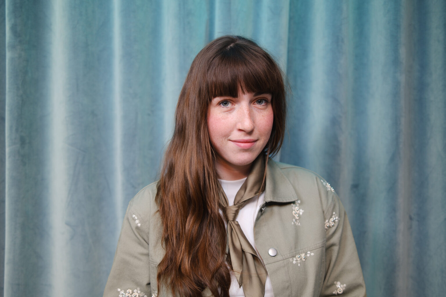 Mikaela st&aring;r framf&ouml;r en bl&aring;turkos gardin.