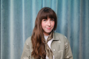 Mikaela står framför en blåturkos gardin.