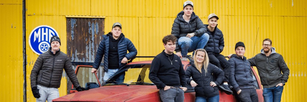 En grupp människor framför en bil utanför en lokal.